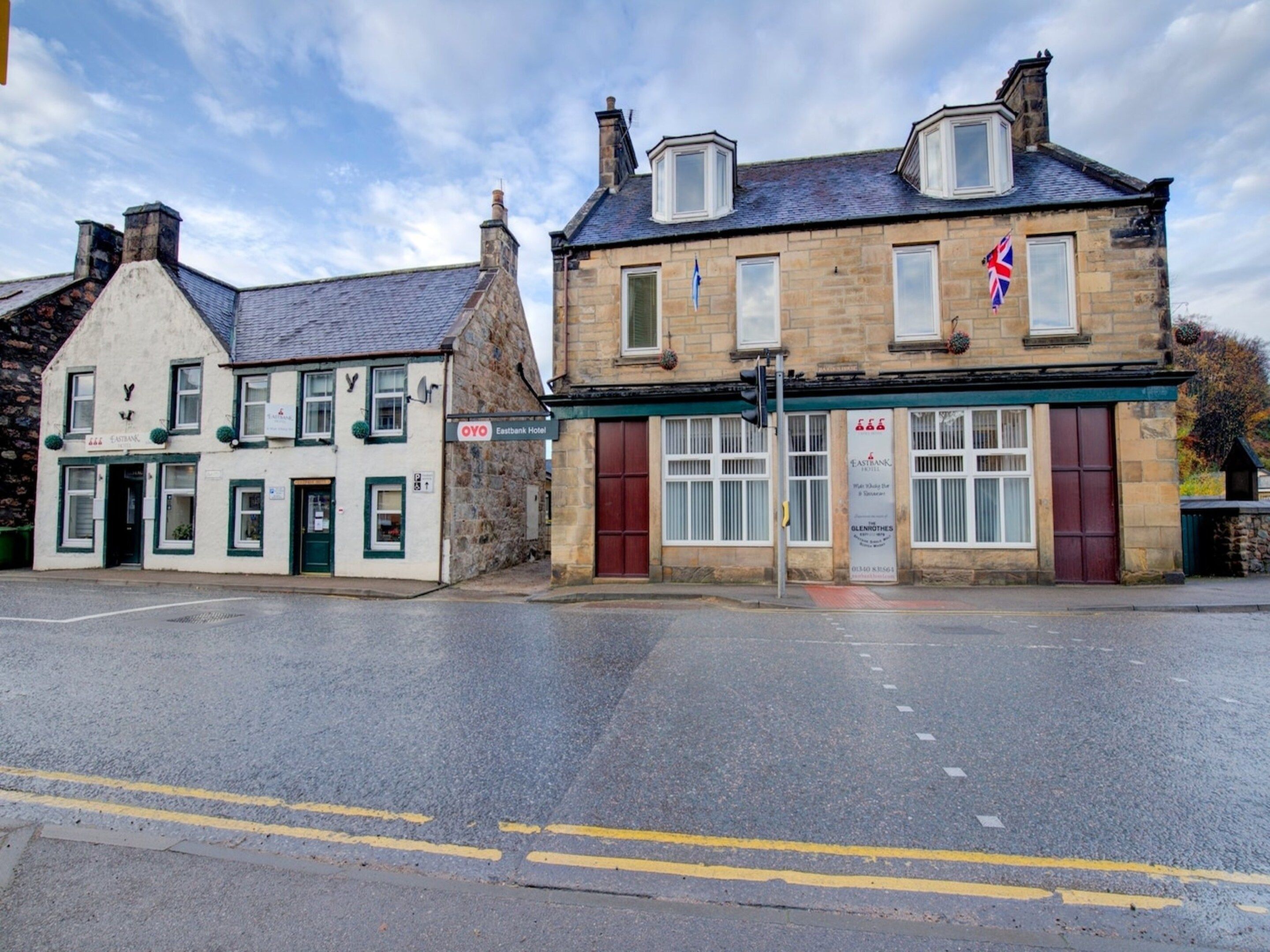 A two-story hotel with a traditional stone facade, a red door, and a British flag.