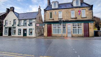 A two-story hotel with a traditional stone facade, a red door, and a British flag.