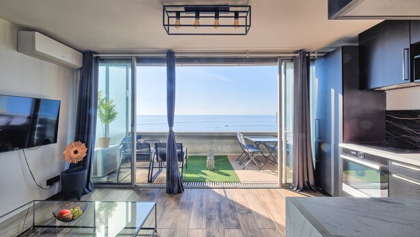 A modern living room with a large TV, a glass coffee table, and a view of the ocean. - "Horizon Bleu" One-bedroom apartment with balcony, ocean view, pool, and parking (Cap-d'Ail)