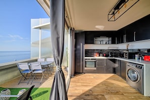 Una cocina moderna con vistas al mar, lavadora y zona de comedor con sillas.