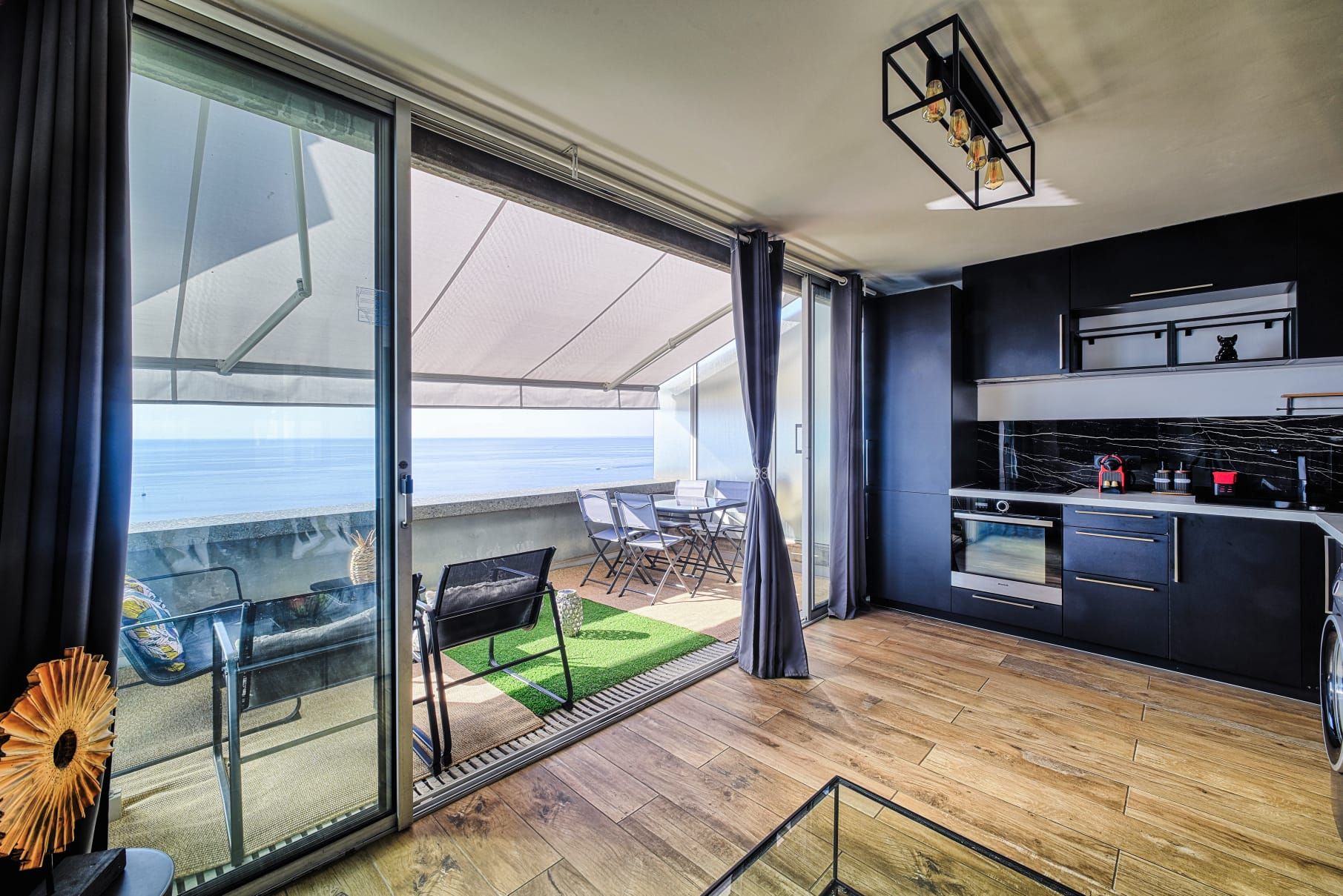 Une cuisine moderne avec vue sur l’océan, un coin repas avec une table et des chaises, et une porte-fenêtre coulissante donnant sur un balcon.