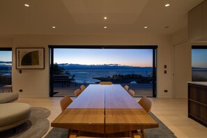 Ein stilvolles Esszimmer mit einem langen Tisch und Stühlen, großen Fenstern mit Blick auf das Meer und die Hügel sowie einem minimalistischen Design.
