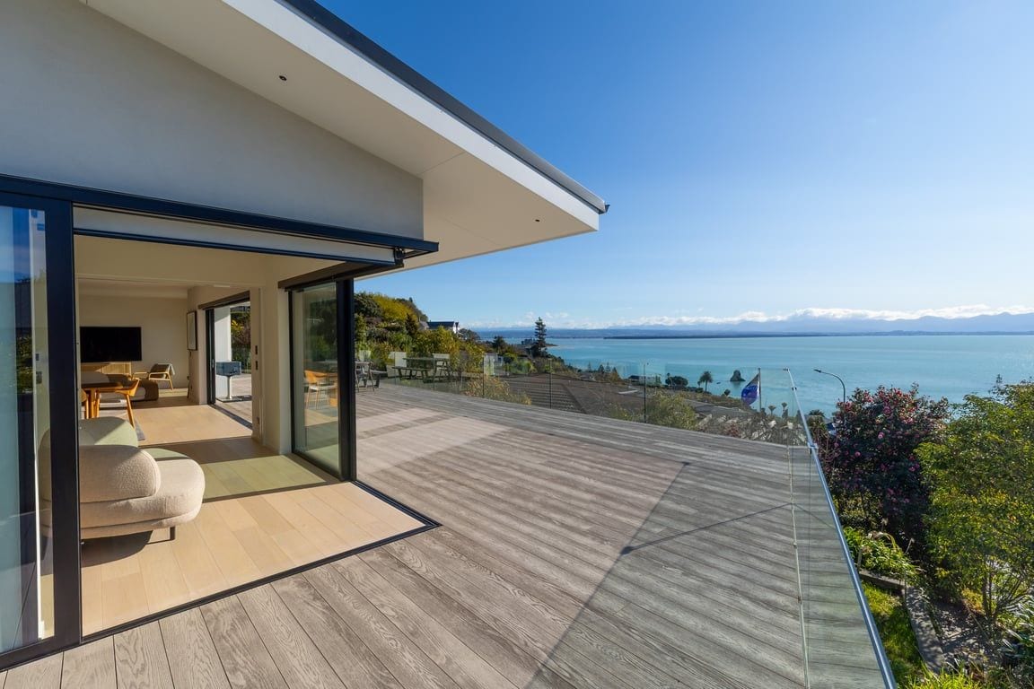 A modern house with a wooden deck and a glass door leading to an outdoor seating area.