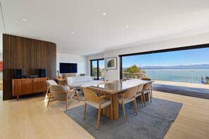 A modern living room with a dining area, large windows, and a view of the sea. - Porto Sanctuary | Tranquil Coastal Luxury with Sweeping Views (Nelson)