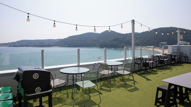 An outdoor seating area with tables and chairs, overlooking a body of water and a beach. - OCEANSUITE (Busan)