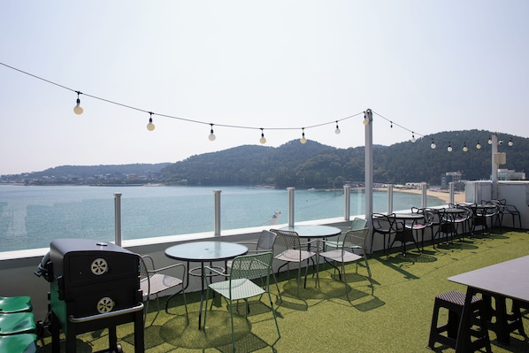 An outdoor seating area with tables and chairs, overlooking a body of water and a beach. - OCEANSUITE (Busan)