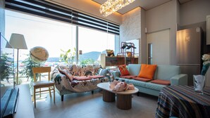 A modern living room with a sofa, armchairs, a coffee table, and a dining table. There is a large window with blinds, a lamp, and a globe on a stand. - OCEANSUITE (Busan)