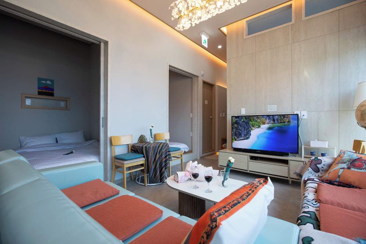 A modern hotel room with a bed, a sofa, a TV, and a dining table with wine glasses.