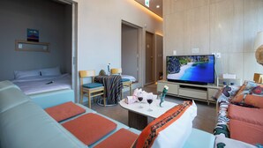A modern hotel room with a bed, a sofa, a TV, and a dining table with wine glasses. - OCEANSUITE (Busan)
