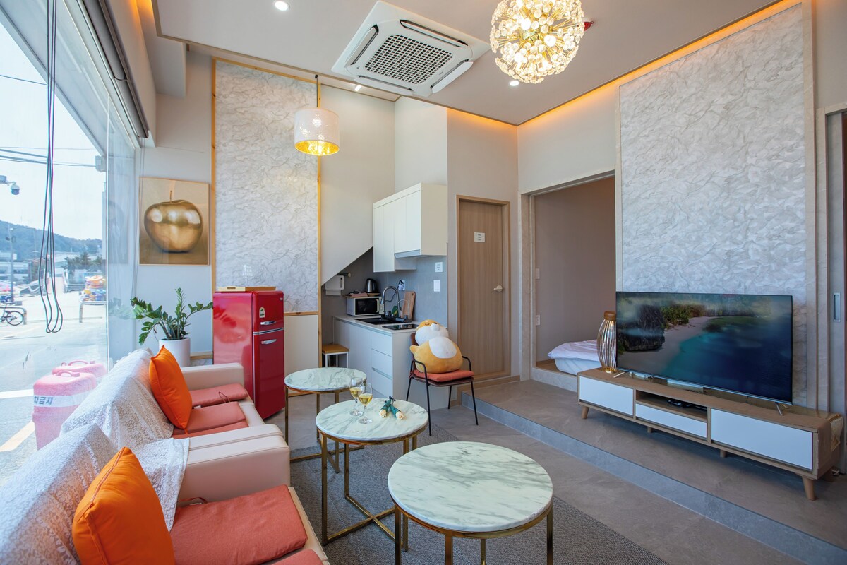 A modern living room with a sofa, coffee table, TV, and a kitchen area.