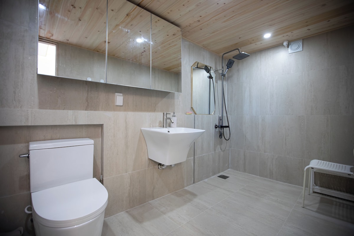 A modern bathroom with a toilet, sink, shower, and a bench.