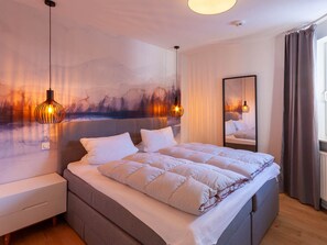 A modern bedroom with a large bed, bedside tables, a wall-mounted mirror, and a painting. - Holiday Apartment With 2 Bedrooms (Braunlage)