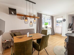 A modern dining area with a wooden table, cushioned chairs, pendant lighting, and a view of the outdoors through a window. - Holiday Apartment With 2 Bedrooms (Braunlage)