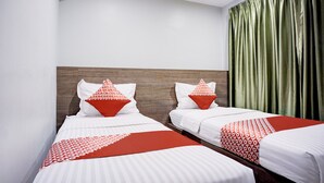 A hotel room with two beds, each with white bedding and red accents, a wooden headboard, and a green curtain.