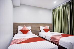 A hotel room with two beds, each with white bedding and red accents, a wooden headboard, and a green curtain.