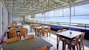 A covered outdoor dining area with tables and chairs, large windows, and a view of the landscape.