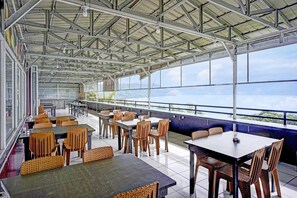 A covered outdoor dining area with tables and chairs, large windows, and a view of the landscape.