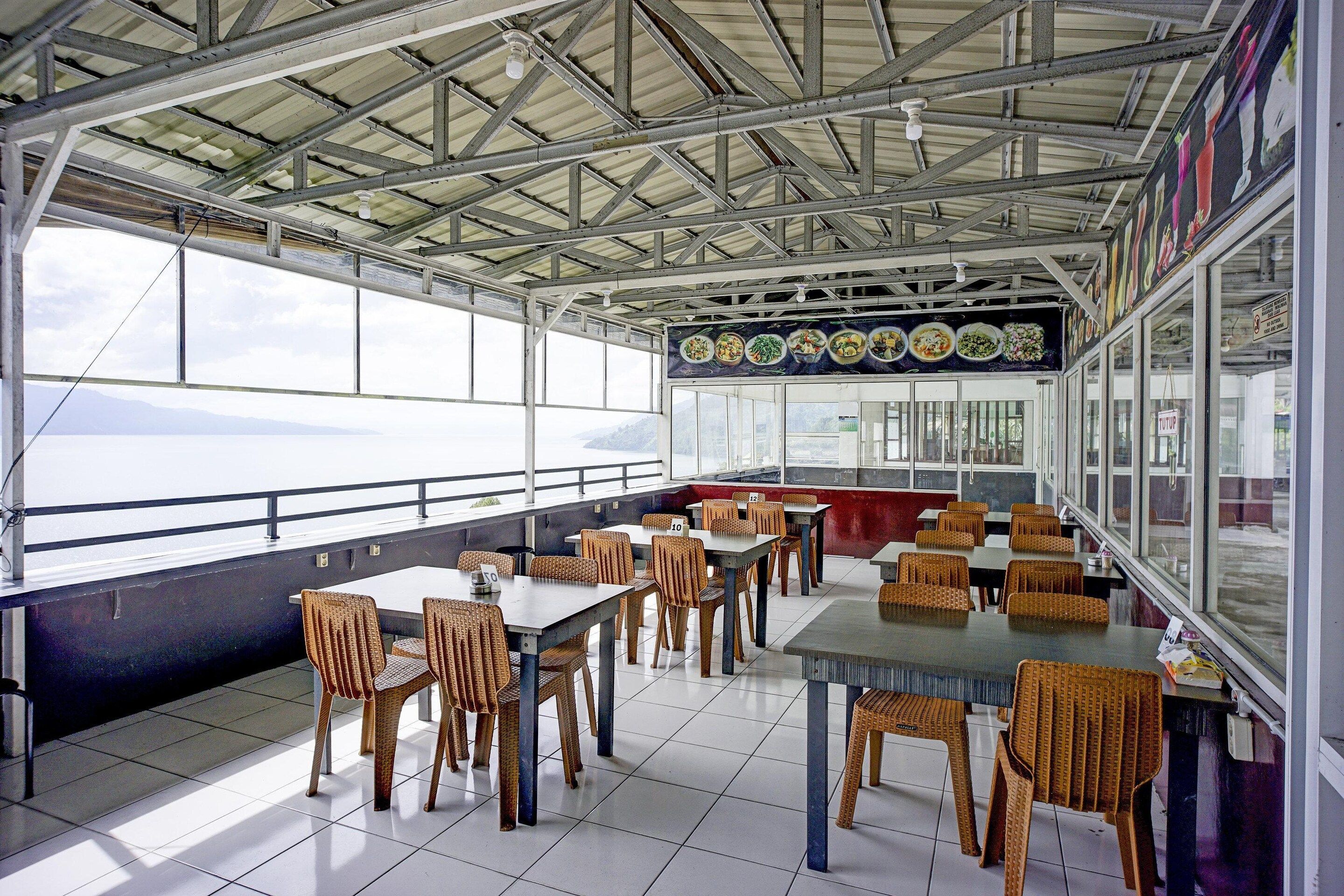 An indoor dining area with tables and chairs, large windows, and a view of the sea.