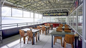 An indoor dining area with tables and chairs, large windows, and a view of the sea.