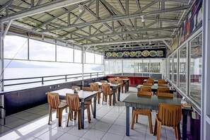 An indoor dining area with tables and chairs, large windows, and a view of the sea.