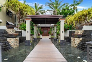 A pathway leading to a covered entrance with a wooden deck, flanked by stone steps and tropical plants. - Belle Escapes Cairns One Condo with Private Pool (Cairns)
