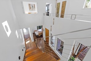 Ein mehrgeschossiges Interieur mit einer Treppe, Holzböden und Kunstwerken an den Wänden.