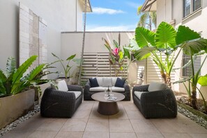 A patio with wicker furniture, a round coffee table, and tropical plants. - Belle Escapes Cairns One Condo with Private Pool (Cairns)