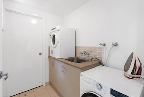 A compact laundry area with a washing machine, a dryer, and a sink. - Belle Escapes Cairns One Condo with Private Pool (Cairns)