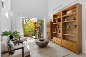 Ein modernes Wohnzimmer mit einer großen Holzregal, einem runden Couchtisch und Blick auf einen Garten durch eine Glastür.