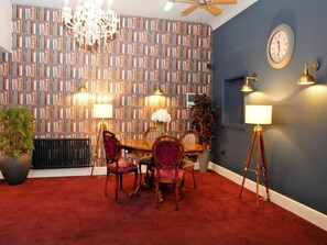 A dining area with a red carpet, a bookshelf wall, a chandelier, and a clock on the wall. - Deluxe Double Room (Crewe)
