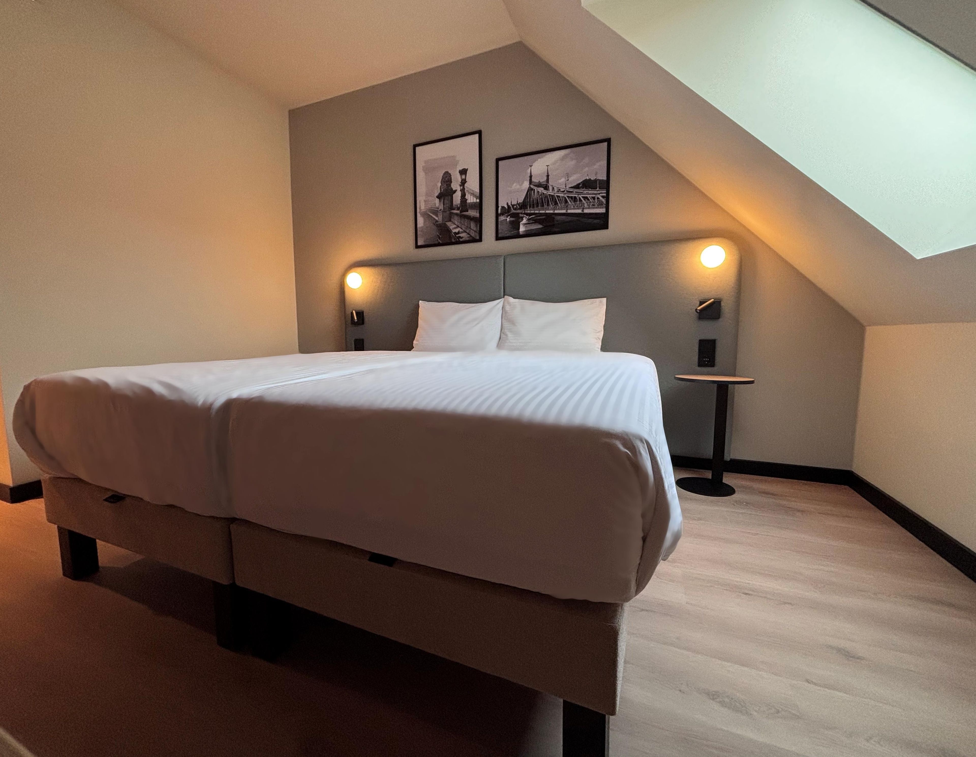Ein Schlafzimmer mit einem großen Bett, zwei Wandleuchten, einem kleinen Tisch und zwei gerahmten Bildern an der Wand.