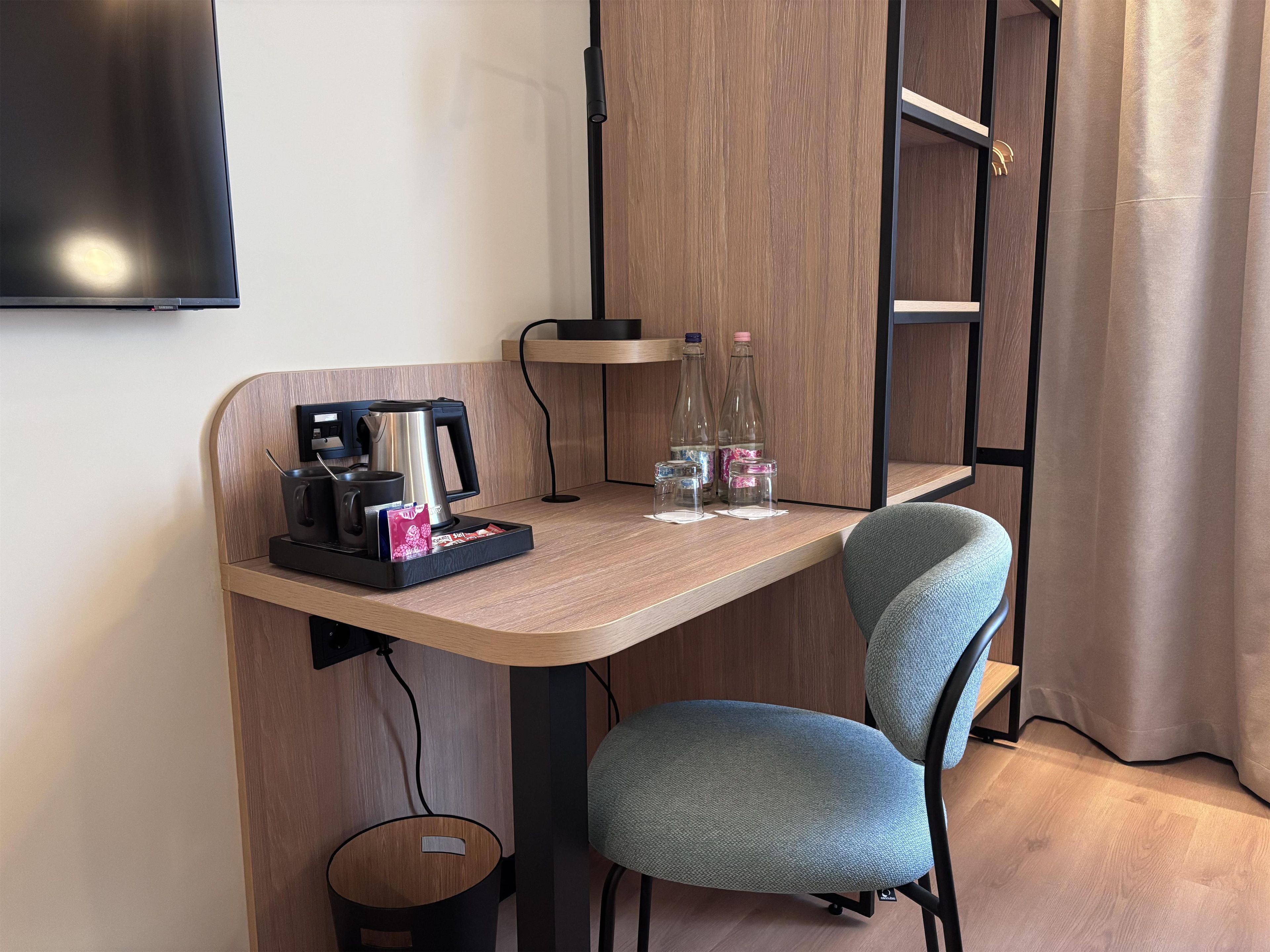 A compact workspace with a coffee maker, bottles, and a chair.
