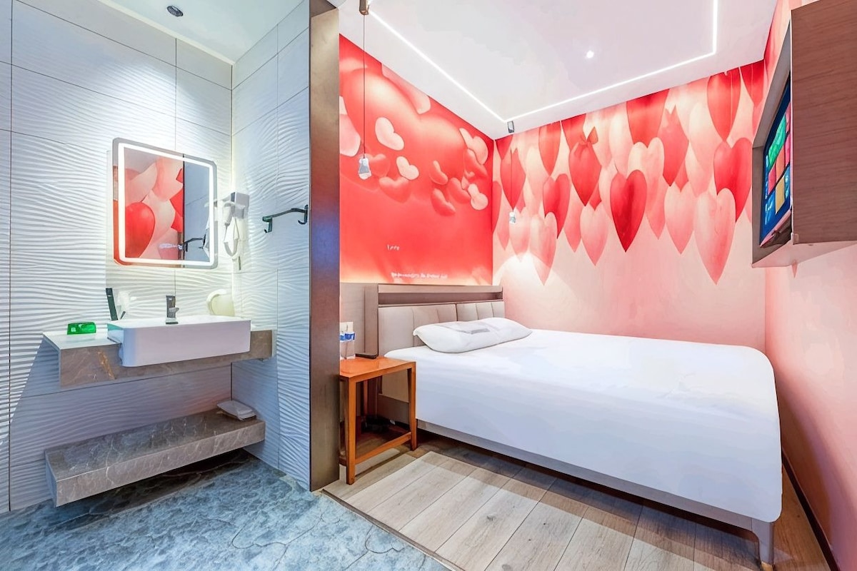 A modern hotel room with a bed, a bedside table, a mirror, and a wall with a heart pattern.