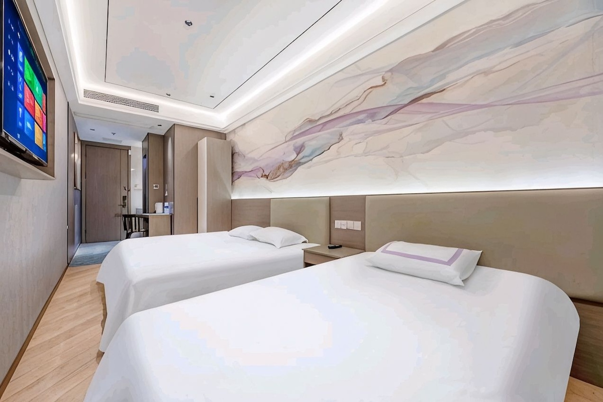 A hotel room with two beds, a large wall-mounted TV, and a marble-like wall design.