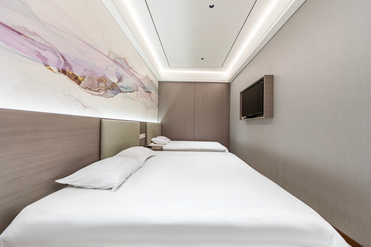 A hotel room with a large bed, a television mounted on the wall, and a ceiling with recessed lighting.