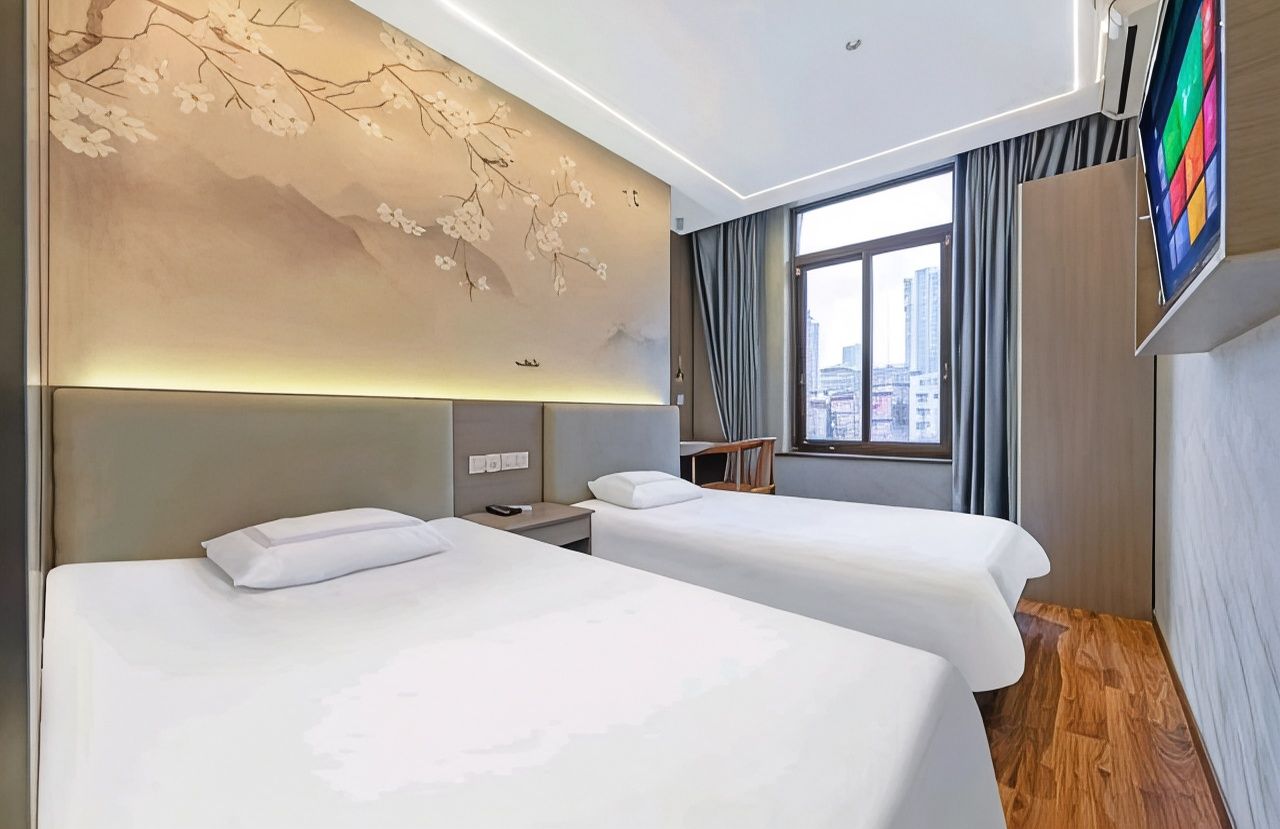 Une chambre d’hôtel avec deux lits, une grande fenêtre et un téléviseur fixé au mur.
