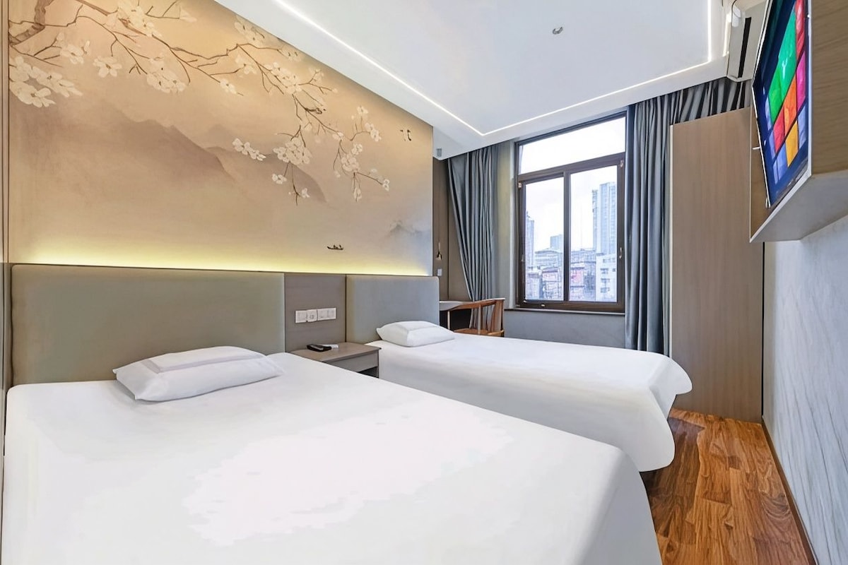 A hotel room with two beds, a large window, and a wall-mounted TV.