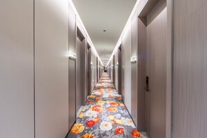 A hotel hallway with a floral carpet, doors on both sides, and a sign indicating room numbers.