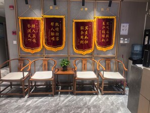 A seating area with wooden chairs and a small table, a water dispenser, and a sign with Chinese characters. - JINOUWANGUO HOTEL (Huangpu District)