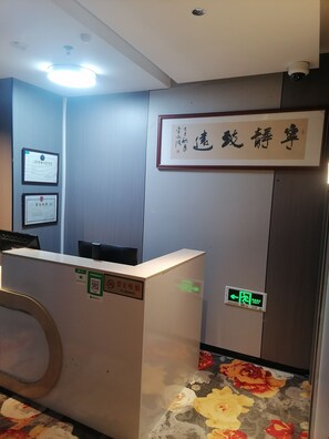 A reception desk with a 'No Smoking' sign, framed certificates on the wall, and a floral carpet.