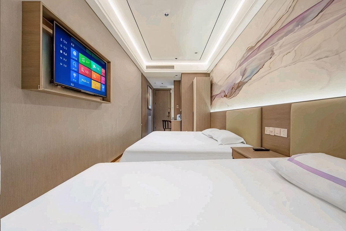 A hotel room with a bed, bedside table, and a wall-mounted TV displaying a colorful interface.