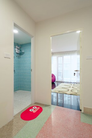 Pasillo de hotel con baño que presenta azulejos azules estampados y una zona de ducha.