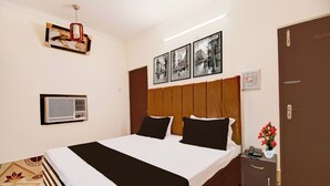Une chambre d’hôtel comprenant un lit, une table de chevet, un téléphone, un vase avec des fleurs et un climatiseur fixé au mur.