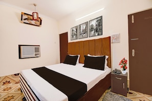 A hotel room with a bed, a bedside table, a telephone, a vase with flowers, and a wall-mounted air conditioner. - Hotel O Benia Park Formerly Parv (Varanasi)
