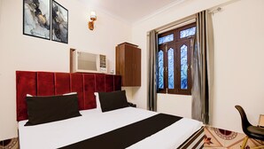 Une chambre d’hôtel comprenant un lit, une armoire, une fenêtre avec des rideaux et un climatiseur fixé au mur.