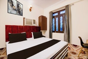 A hotel room with a bed, a wardrobe, a window with curtains, and a wall-mounted air conditioning unit. - Hotel O Benia Park Formerly Parv (Varanasi)