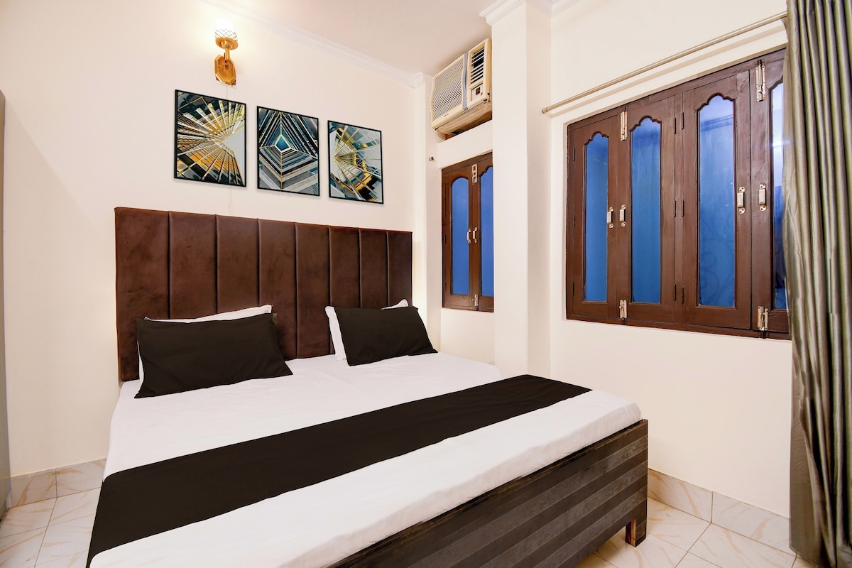 A hotel room with a bed, a headboard, a window with curtains, and wall-mounted artwork.