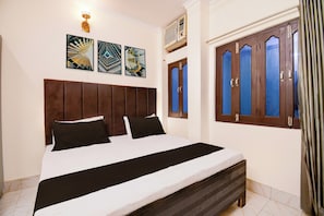 A hotel room with a bed, a headboard, a window with curtains, and wall-mounted artwork. - Hotel O Benia Park Formerly Parv (Varanasi)