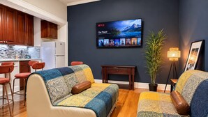 Un salon moderne avec un canapé, un téléviseur affichant l’interface de Netflix, une petite table et une plante en pot.