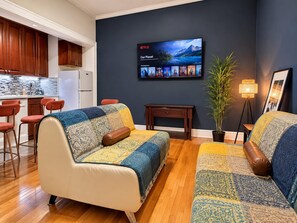 Ein modernes Wohnzimmer mit einer Couch, einem Fernseher, der eine Netflix-Oberfläche zeigt, einem kleinen Tisch und einem Blumentopf.